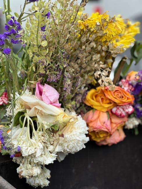 A close-up of a vibrant floral arrangement featuring a variety of freshly cut flowers, including white and pink roses, yellow and purple wildflowers, and clusters of delicate blossoms. The bouquet sho